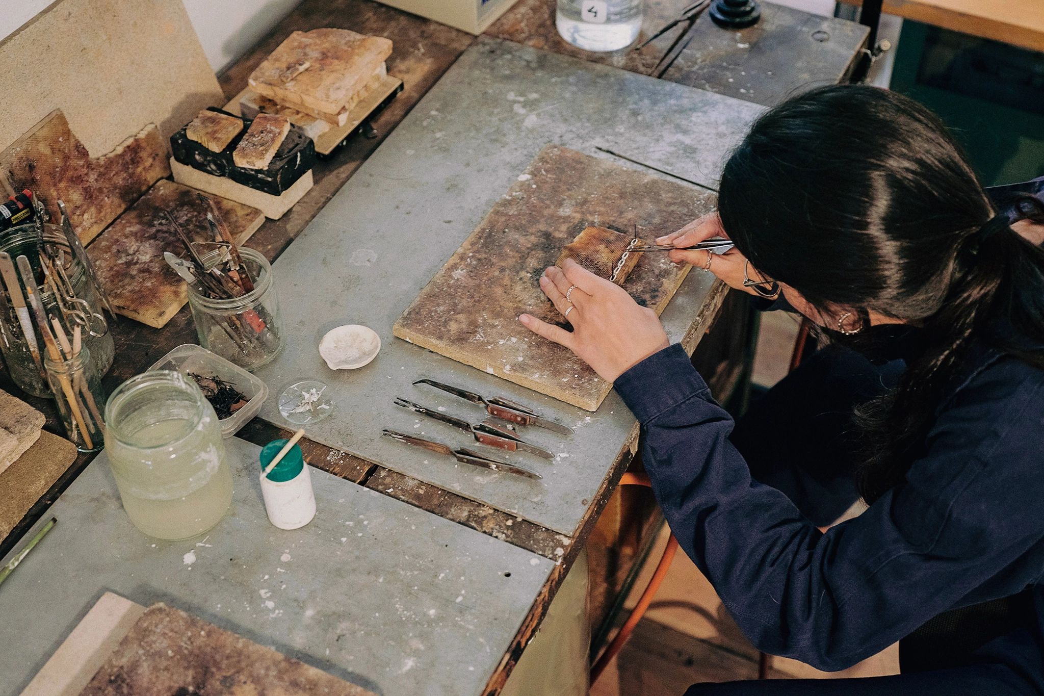 A person leans over a workshop table with woodworking tools in hand