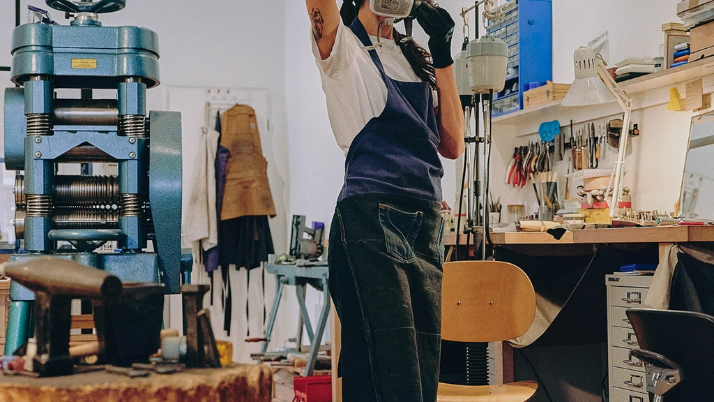 A woman in denim overalls attaches an industrial mask over her head