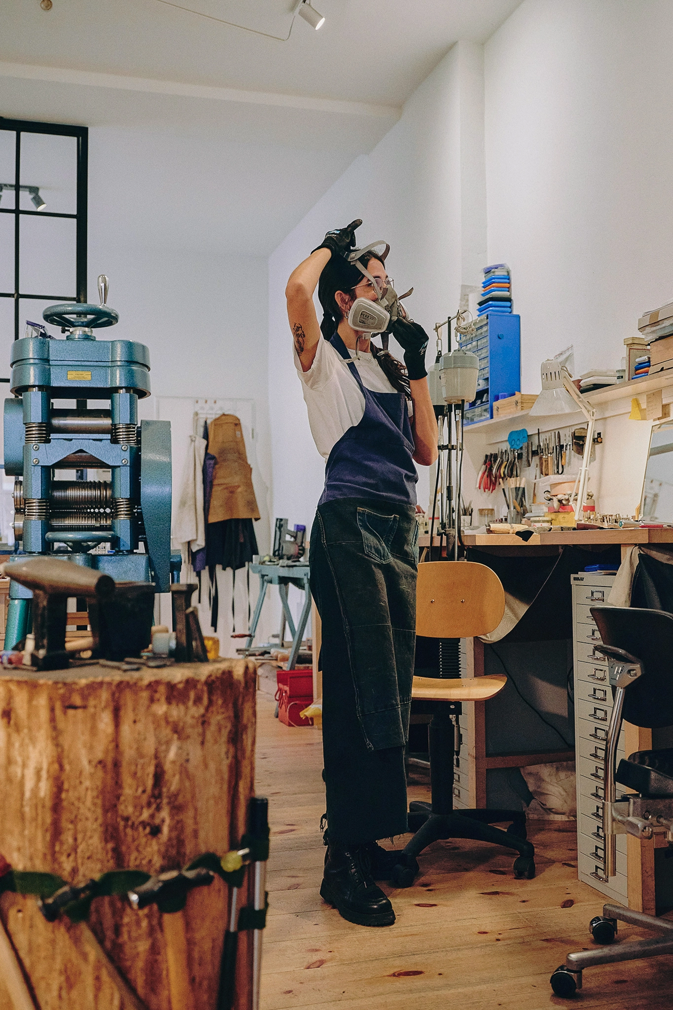 A woman in denim overalls attaches an industrial mask over her head