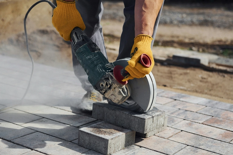 A pair of hands in work gloves hold a circular saw to cut a brick