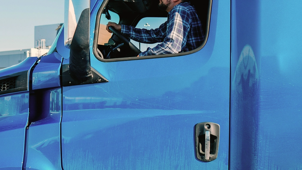 Close up side view of a man driving a blue truck against a blue sky