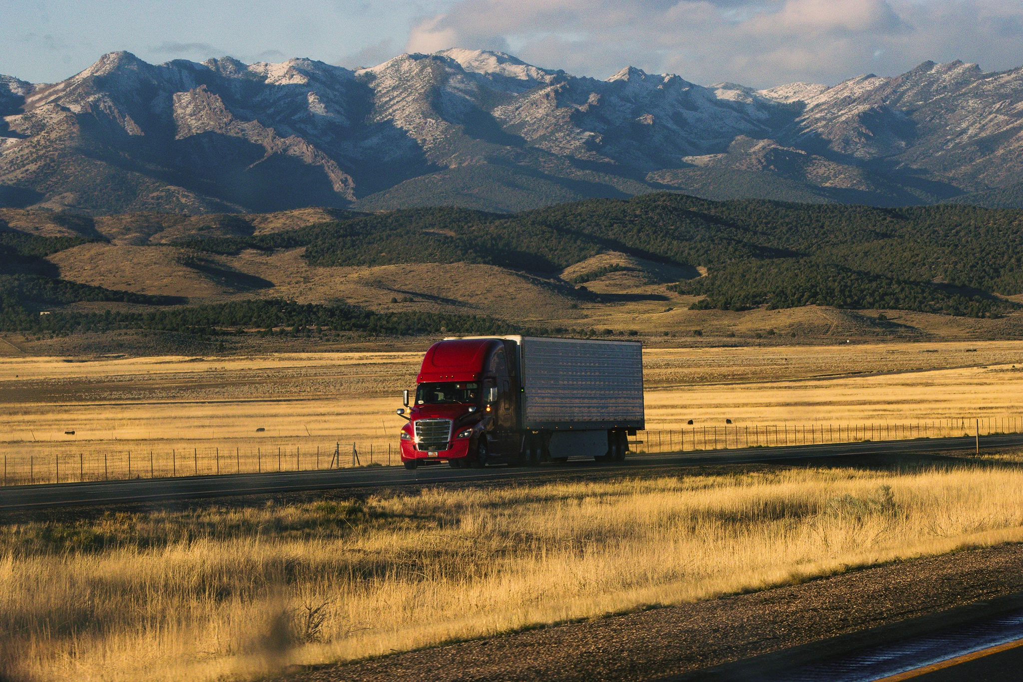 A truck drives down a road with snow-capped mountains in the background