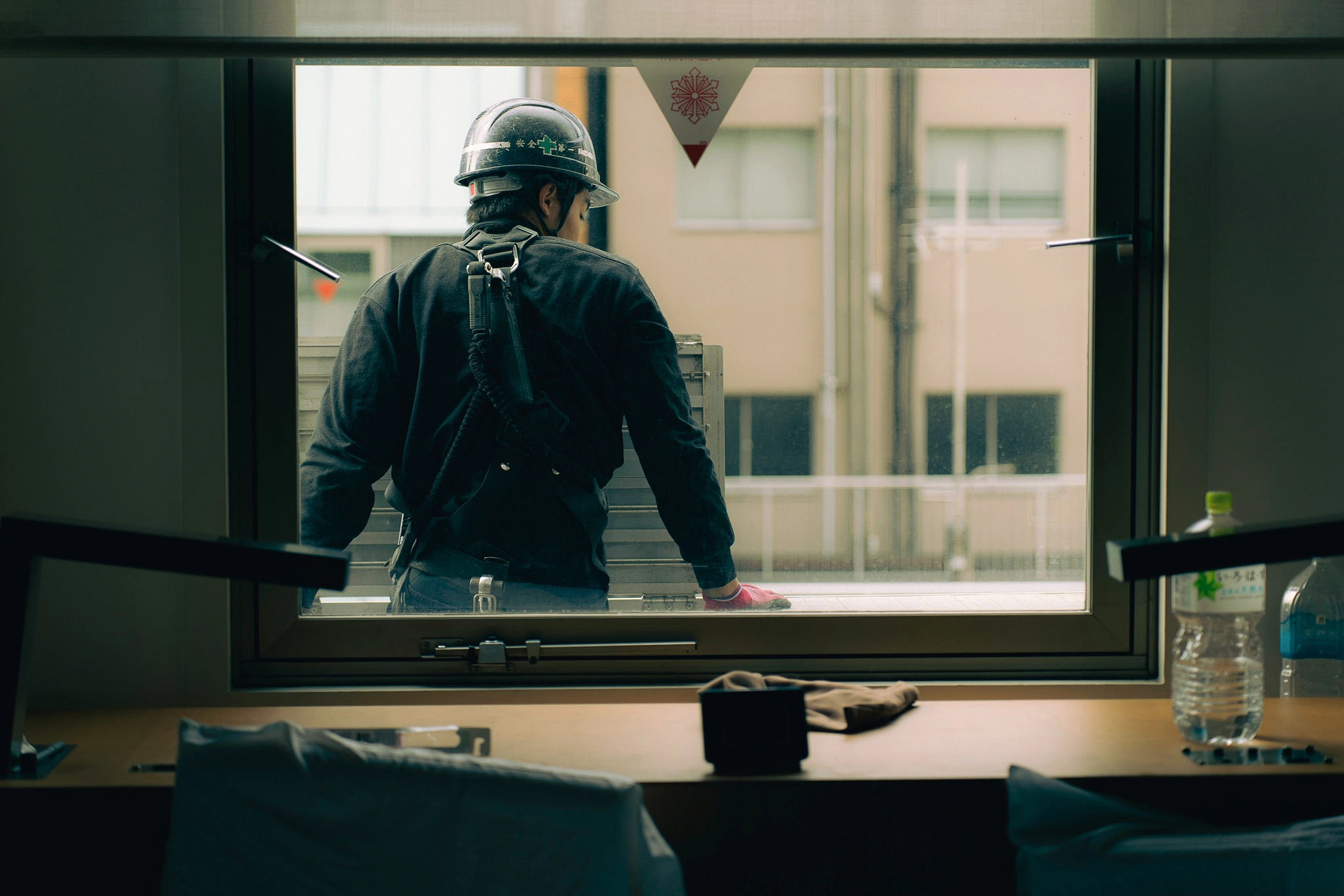A man in a hard hat leans with his back against a window frame