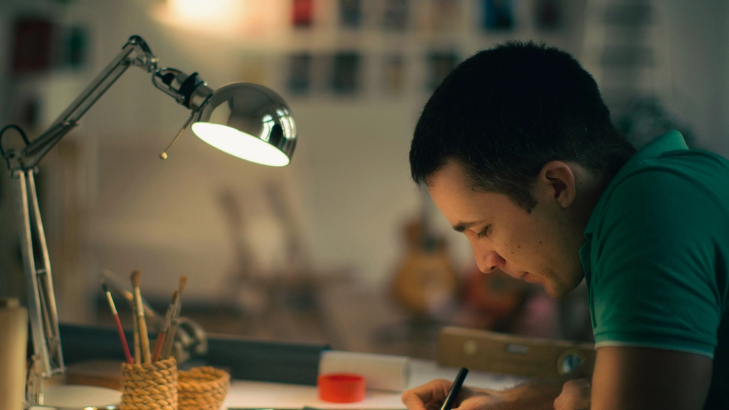 Man bent over a drafting table working with a desk lamp shining on his work