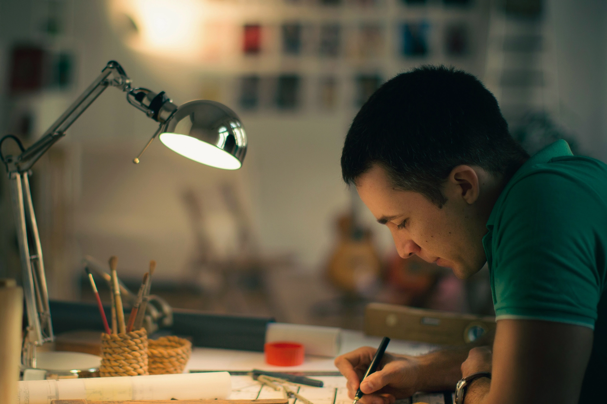 Man bent over a drafting table working with a desk lamp shining on his work