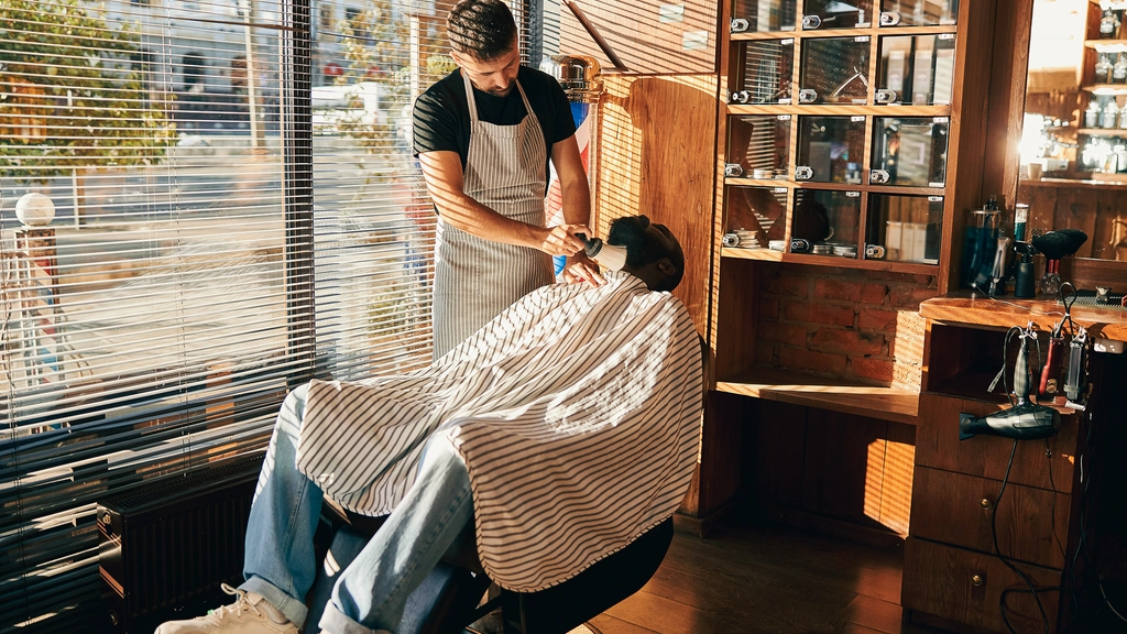 A barber prepares to cut his clients hair, who is seated in a barber chair