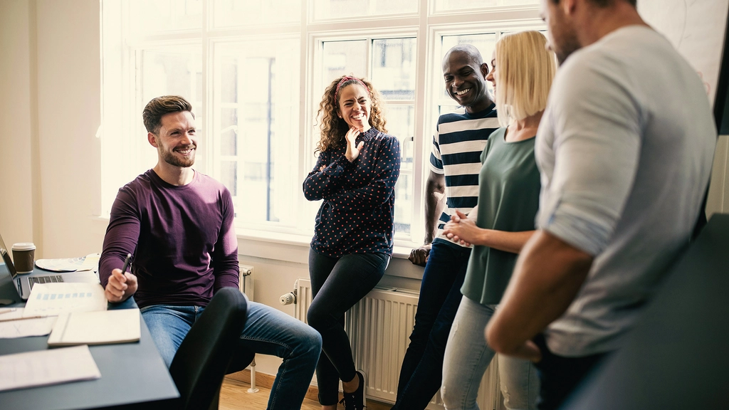 Five colleagues at work making small talk and laughing