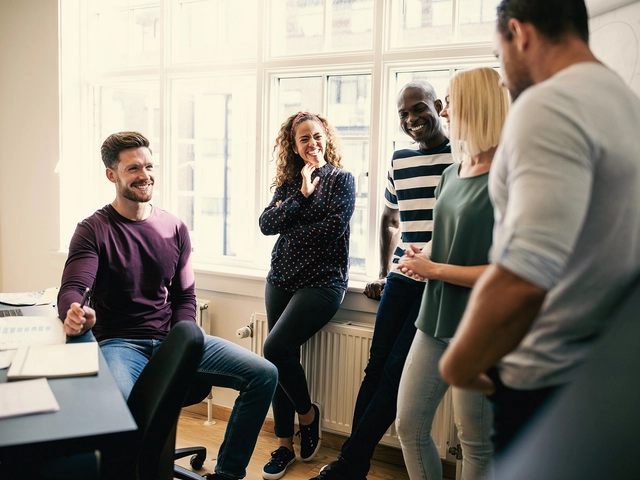 Five colleagues at work making small talk and laughing