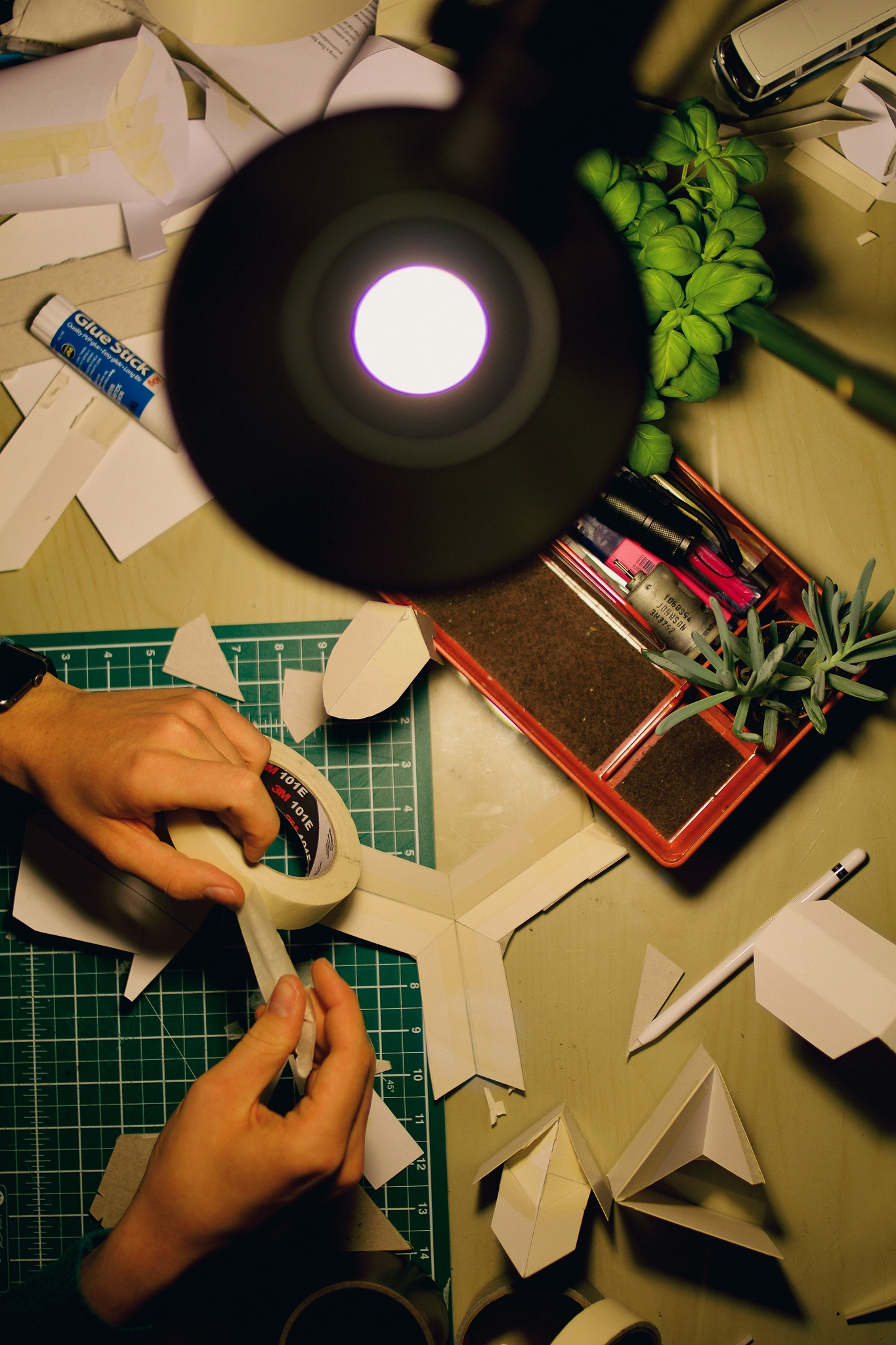 An overhead view of a desk with a light and a person's hands working with objects