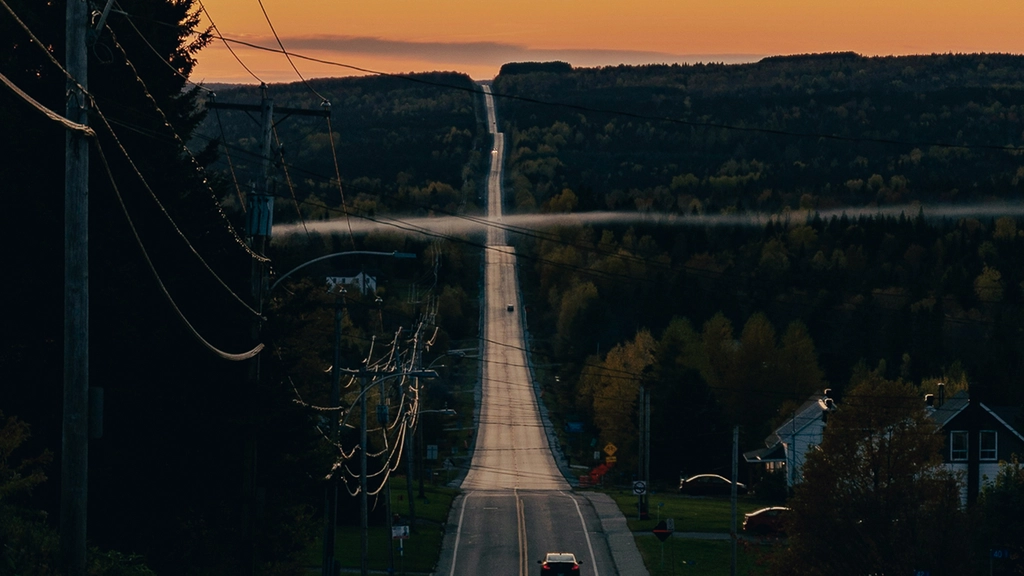 A card drives into the sunset on a long, hilly road.