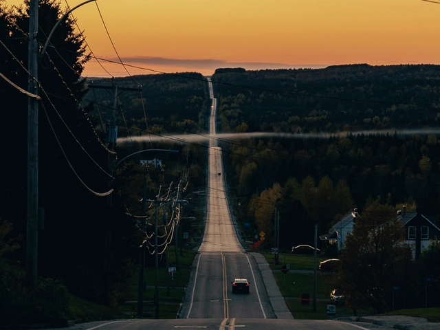 A card drives into the sunset on a long, hilly road.