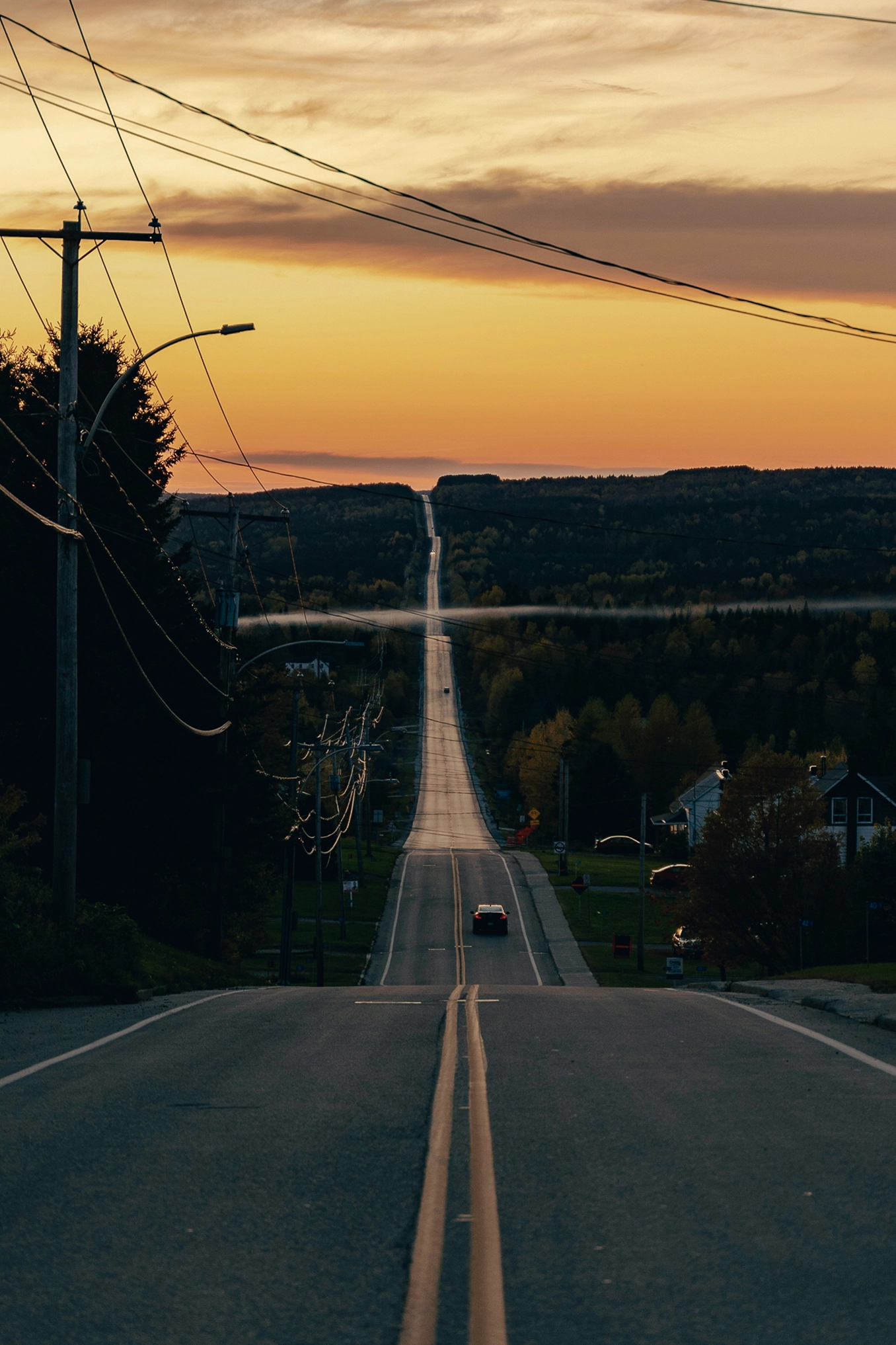 A card drives into the sunset on a long, hilly road.
