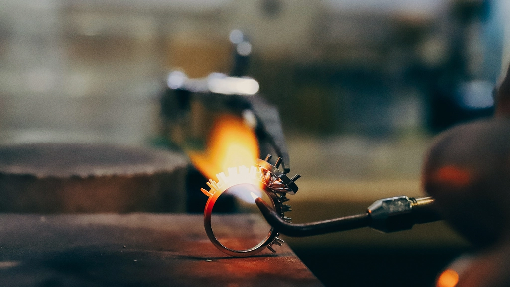 A metalsmith holds a blowtorch to a circle