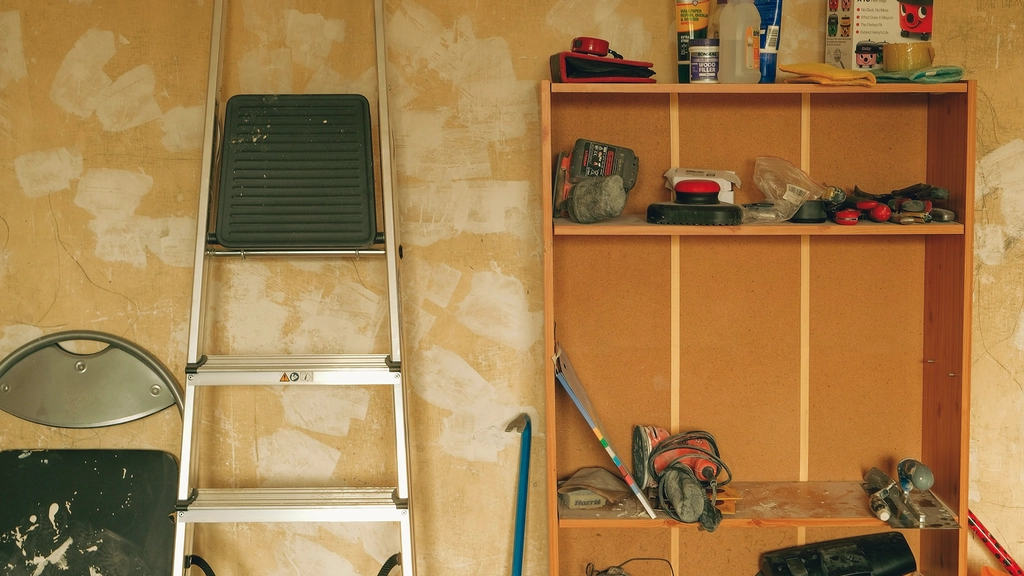 A wall with a ladder leaned up against it and shelving filled with tools