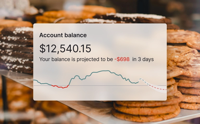 Bakery display of cookies with account balance dashboard showing projected negative cash flow.