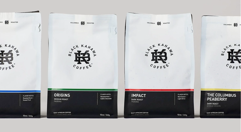 Four bags of Black Kahawa Coffee labeled Origins, Impact, and The Columbus Peaberry, featuring clean white packaging with colored accents.