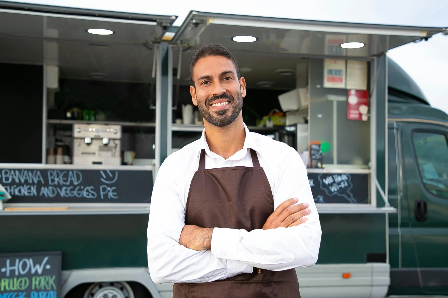 man wearing apron standing in front of a food truck
