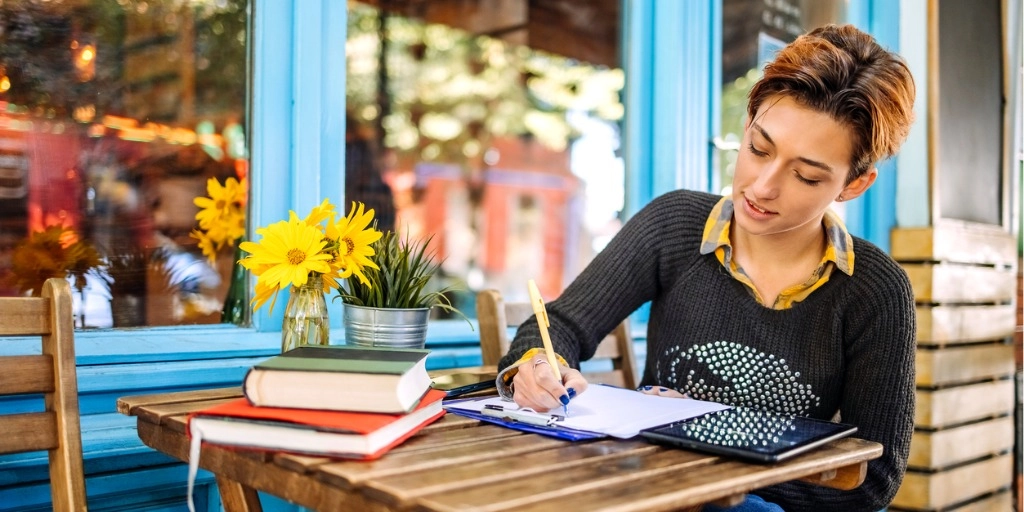 Small business owner sitting at a cafe table reviewing her possible tax write offs on a tablet