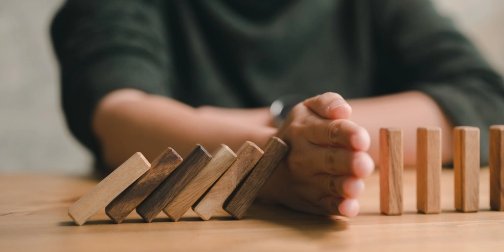 A set of dominos where half are falling and a hand is protecting the other half from going down