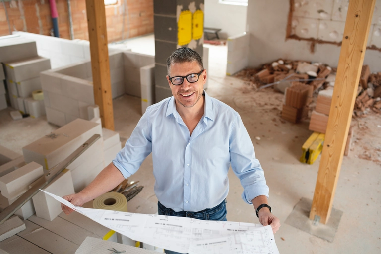 man with black glasses and blue shirt checking plans and construction progress on building site used to illustrate article about high risk business loans