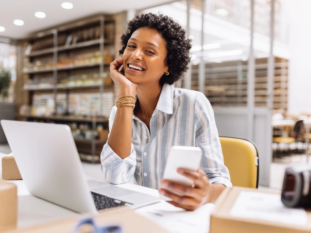 business owner smiling with laptop and cell phone to represent checking business credit