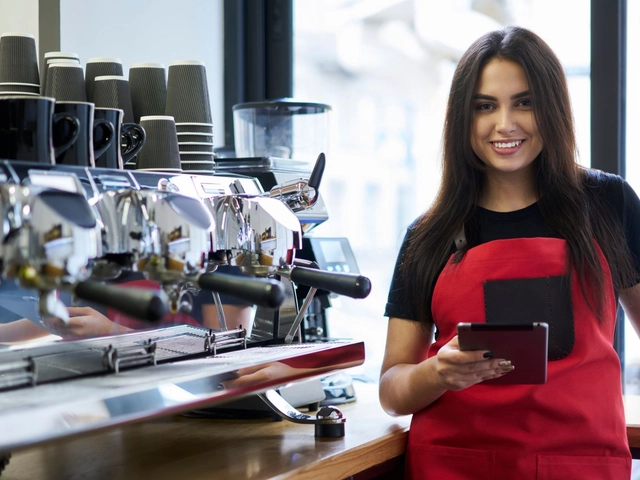 Smiling woman with long dark hair wearing a red apron standing by expresso bar with tablet in hand used to illustrate article about highest possible business credit scores