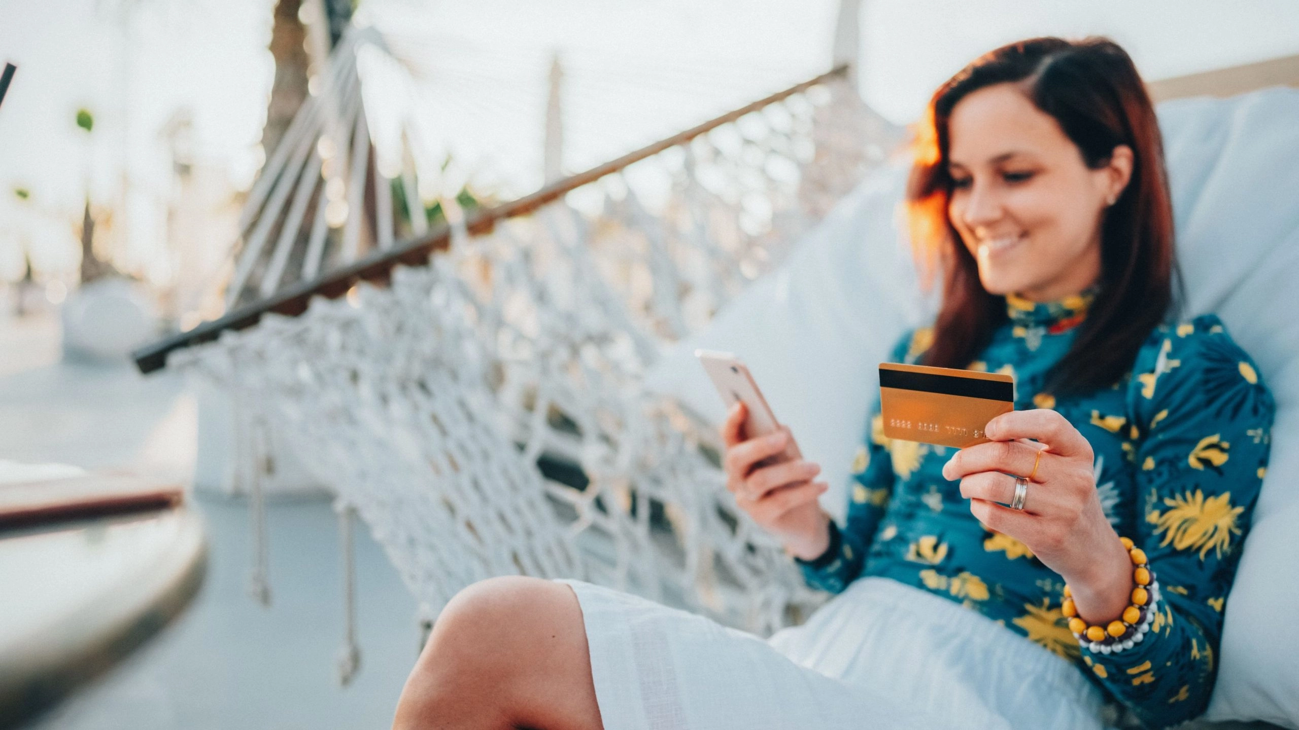 Woman small business owner sitting in a hammock making an online purchase with a credit card from her phone