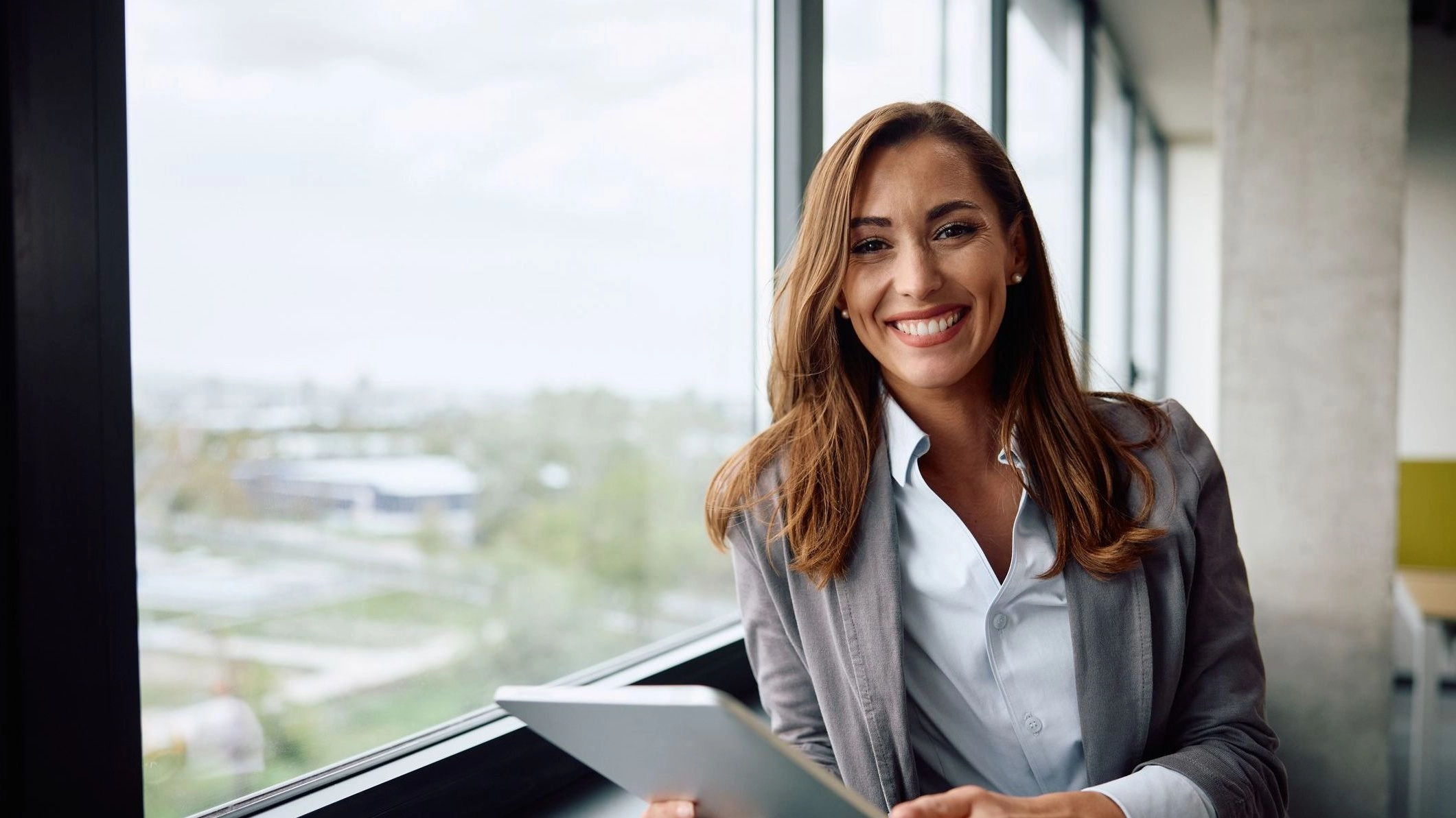 Photo of woman standing by window, smiling and holding a tablet to illustrate article about cash flow forecasting