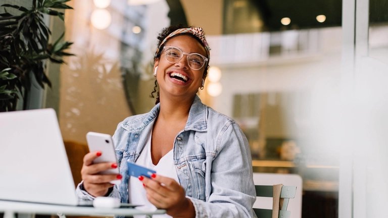 Smiling woman with credit card and cell phone to illustrate article about credit cards for startups