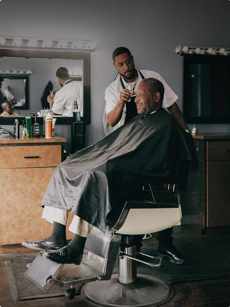 A younger african american man giving a middle aged african american man a haircut