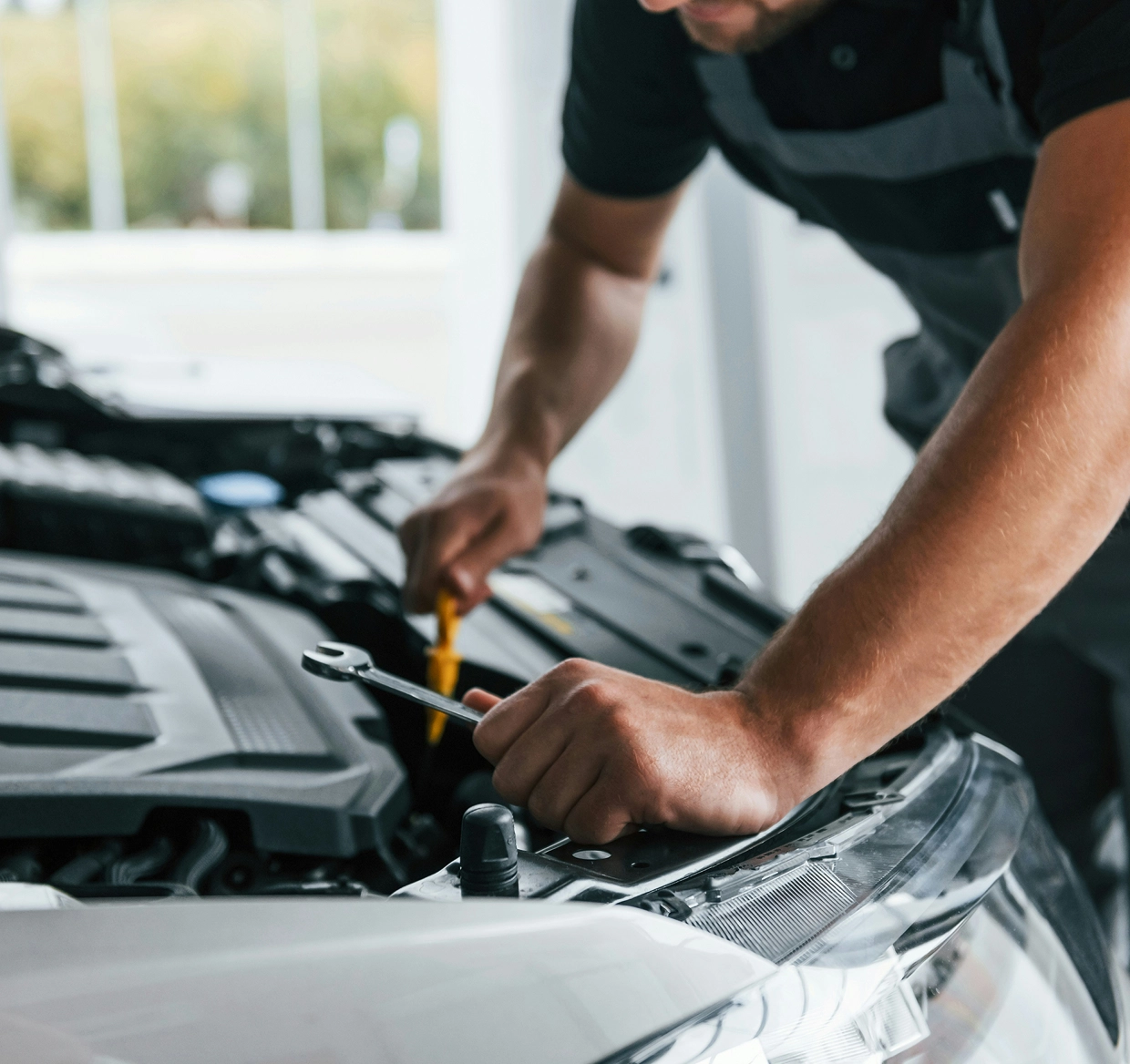 Auto mechanic using a wrench on a car engine in a repair shop.