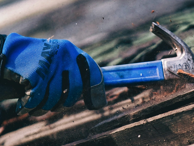 Close-up of a gloved hand using a hammer to break wood during a construction project.