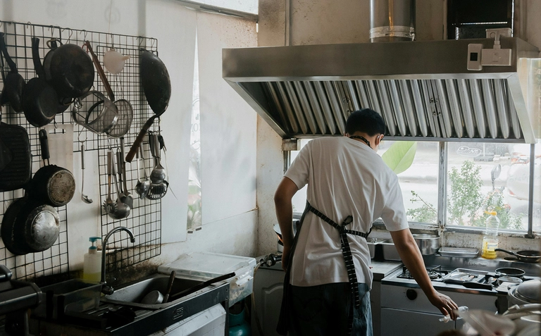 Chef working at a stove in a small kitchen with hanging cookware.