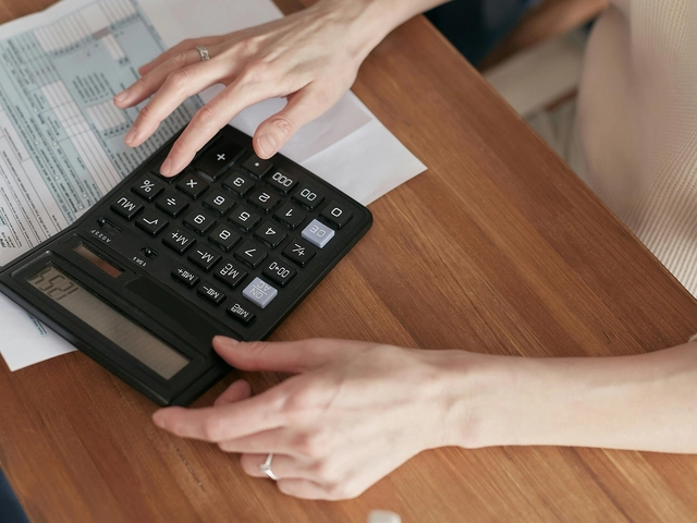 Person using a calculator to review financial documents on a wooden table.