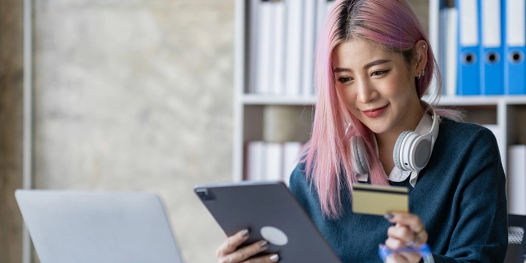 A woman small business owner sitting at a desk with her credit card and looking at an ipad for guidance on how to close a credit card