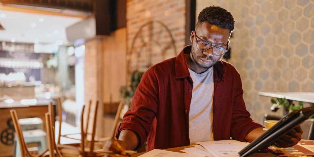 Male coffee shop owner sitting at table working through quarterly taxes