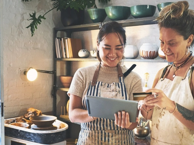 female small business owner holding a revenued business card and looking at an ipad with a co-worker