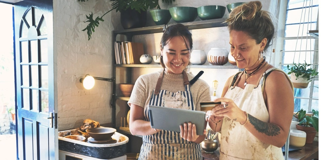female small business owner holding a revenued business card and looking at an ipad with a co-worker