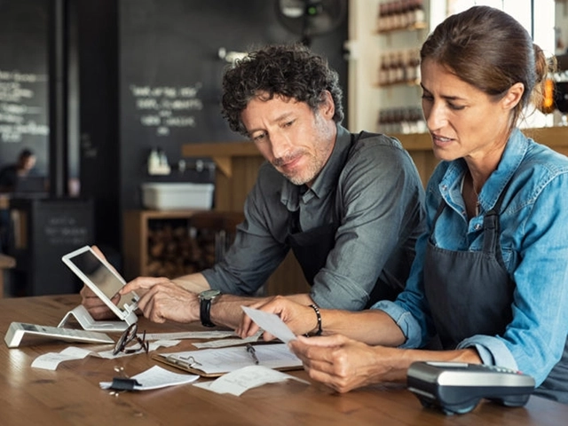 Two people in aprons reviewing receipts and business finances at a café counter.