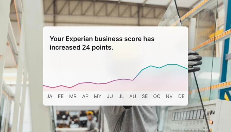 Notification reading 'Your Experian business score has increased 24 points' displayed over a background of a worker handling glass panels in an industrial setting