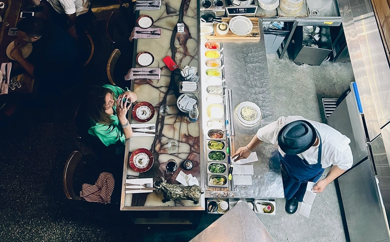 Overhead view of a restaurant kitchen and dining counter with staff preparing food and a customer seated.