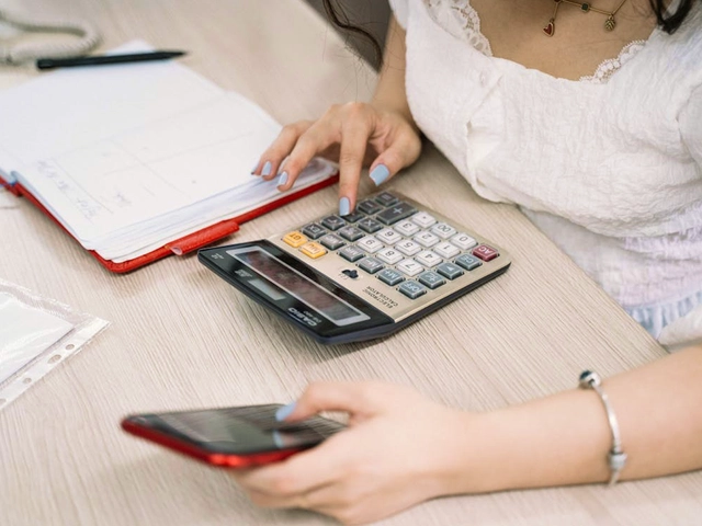 Person using a calculator and smartphone while managing finances at a desk.